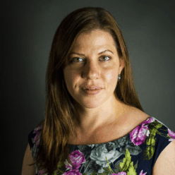 A woman wearing a pink floral dress with brown hair smiling.