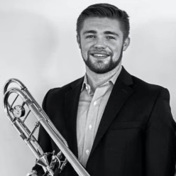 A man wearing a back suit holding a trombone smiling.