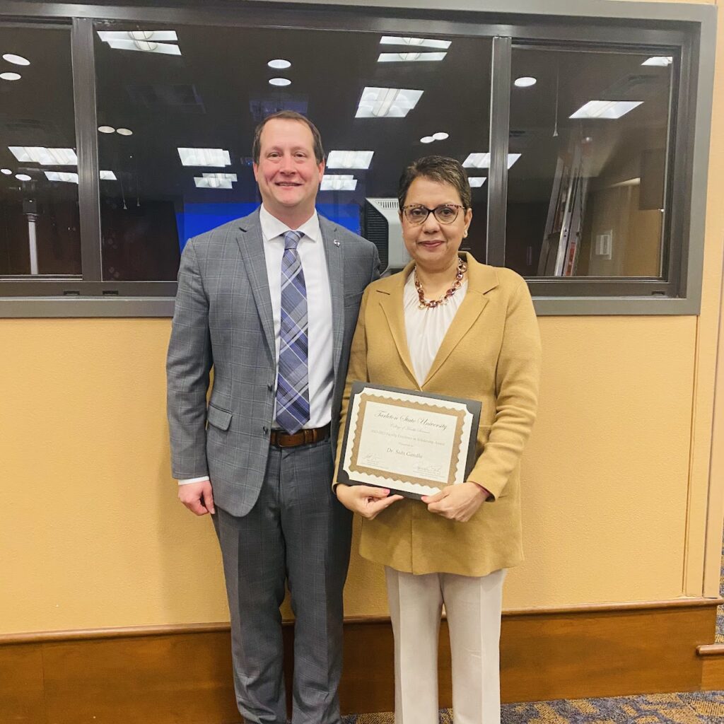 A man wearing a grey suit on the left and a woman wearing a yellow jacket with a white shirt and kaki dress pants on the right. 
