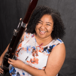 A woman wearing a colorful shirt smiling with an instrument.