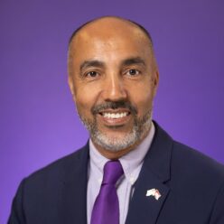 Smiling man in front of purple background.