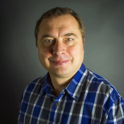 A man wearing a blue plaid shirt smiling.