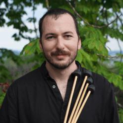 A man with a black shirt and a brown beard smiling.