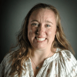 A woman wearing a white shirt with blonde hair smiling.